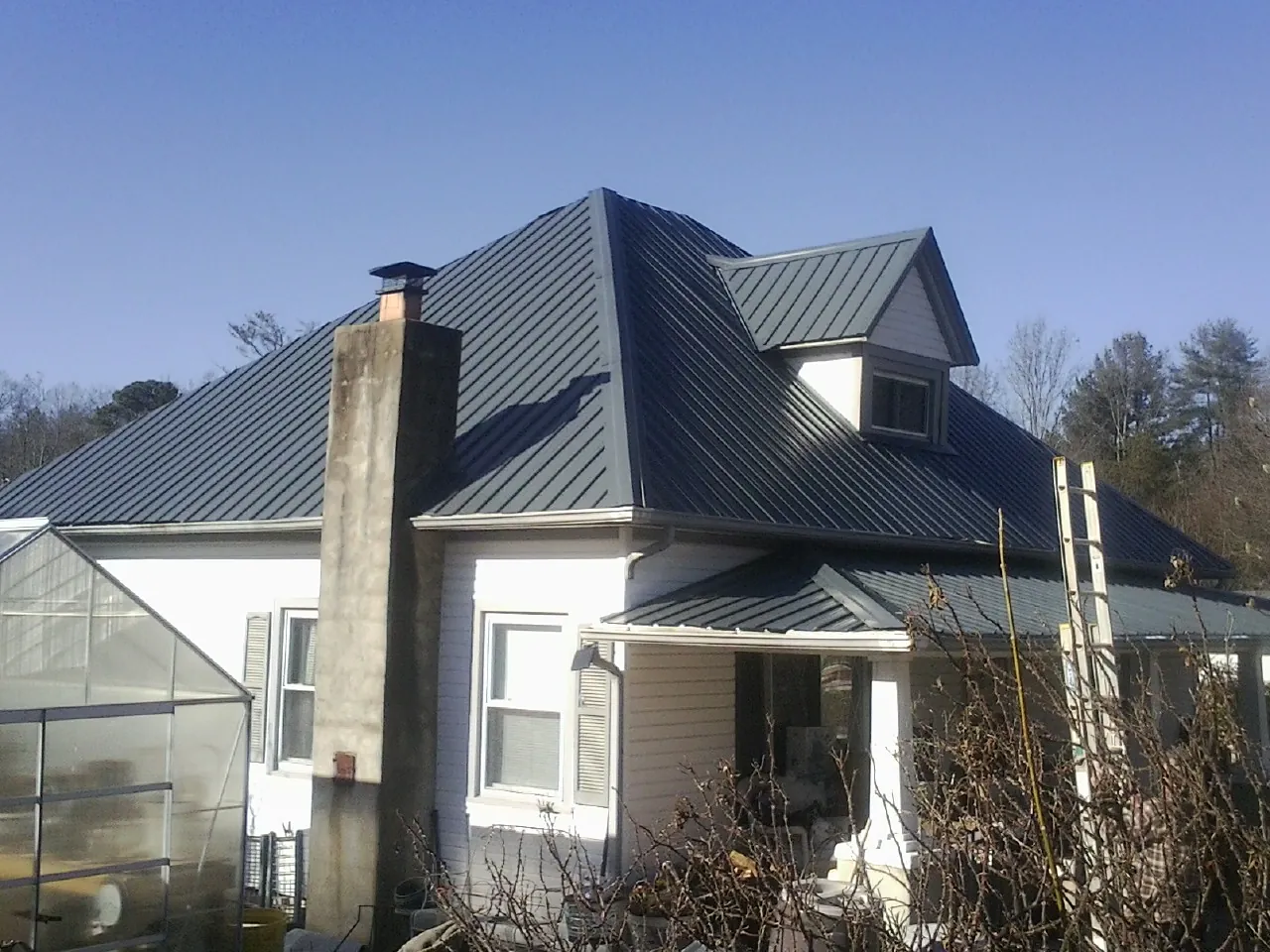 Dark blue standing seam metal roof on a white farmhouse with dormer — Slate & Tile Roof Repair by Roofing Brothers in Blandon