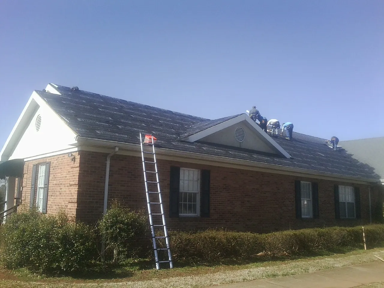 Crew tearing shingles off a brick ranch roof with a ladder set — Emergency Roof Repair work by our crew in Blandon