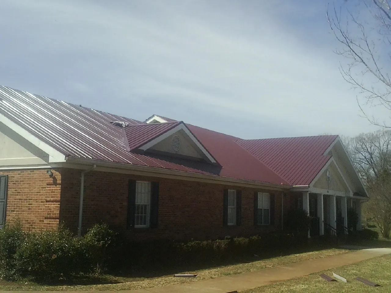 Red metal roof with gabled entries on a long brick building, from a Hail Damage Roof Repair job in Blandon