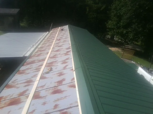 Old rusted panels beside newly installed green metal roofing — Wind Damage Roof Repair by Roofing Brothers in Blandon
