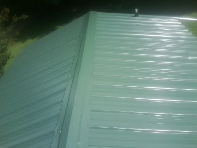 New green metal panels meeting at the ridge of a roof — Flat Roof Repair work by our crew in Blandon