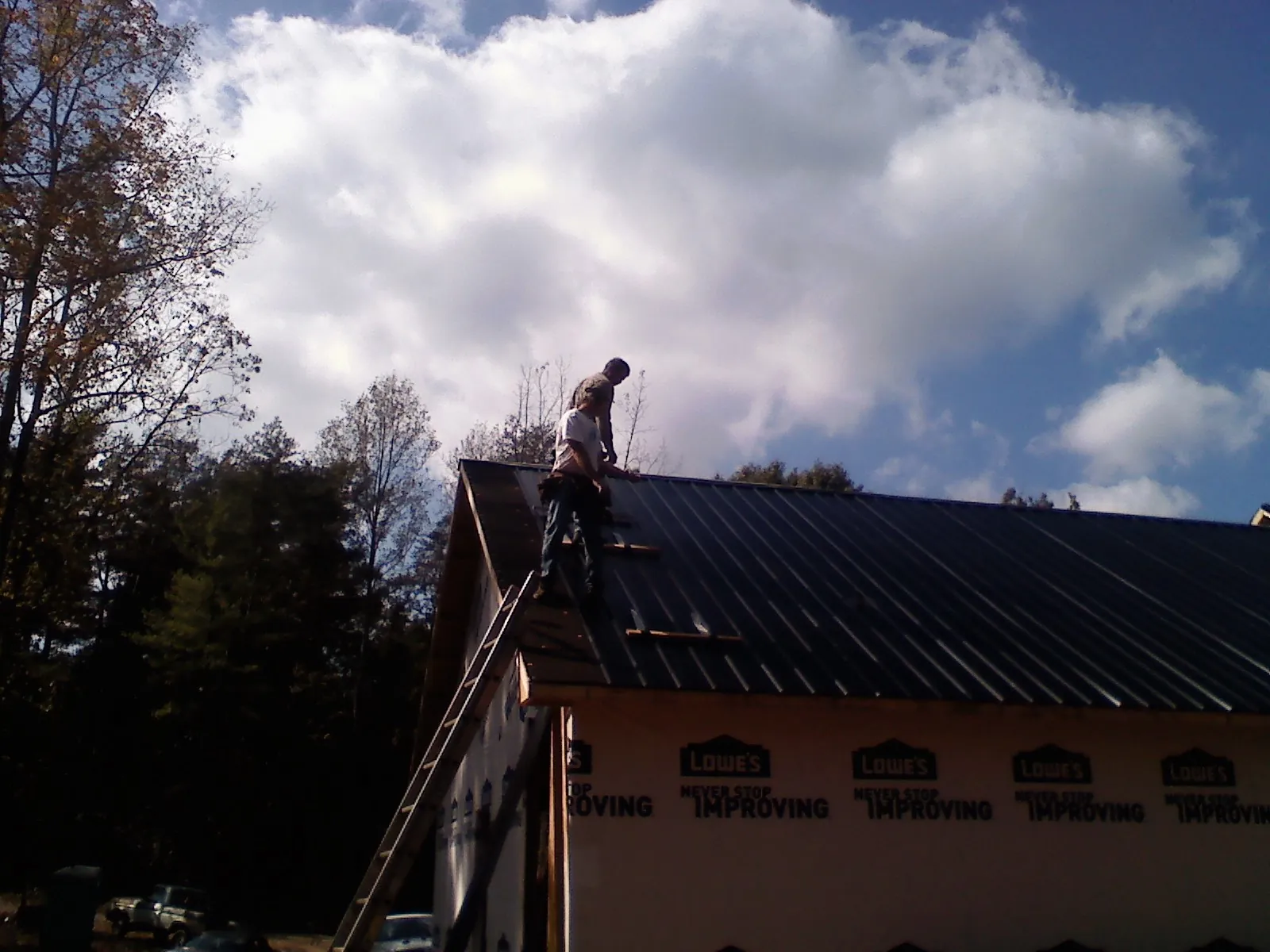 Roofer fastening dark metal panels high against a cloudy sky, from a Roof Inspection job in Blandon
