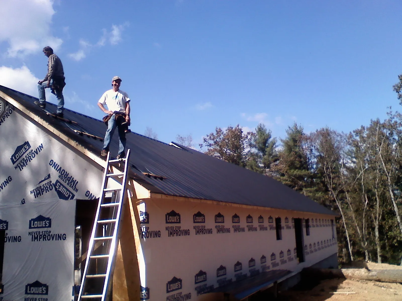 Two roofers standing on a long dark metal roof over a wrapped building in Blandon