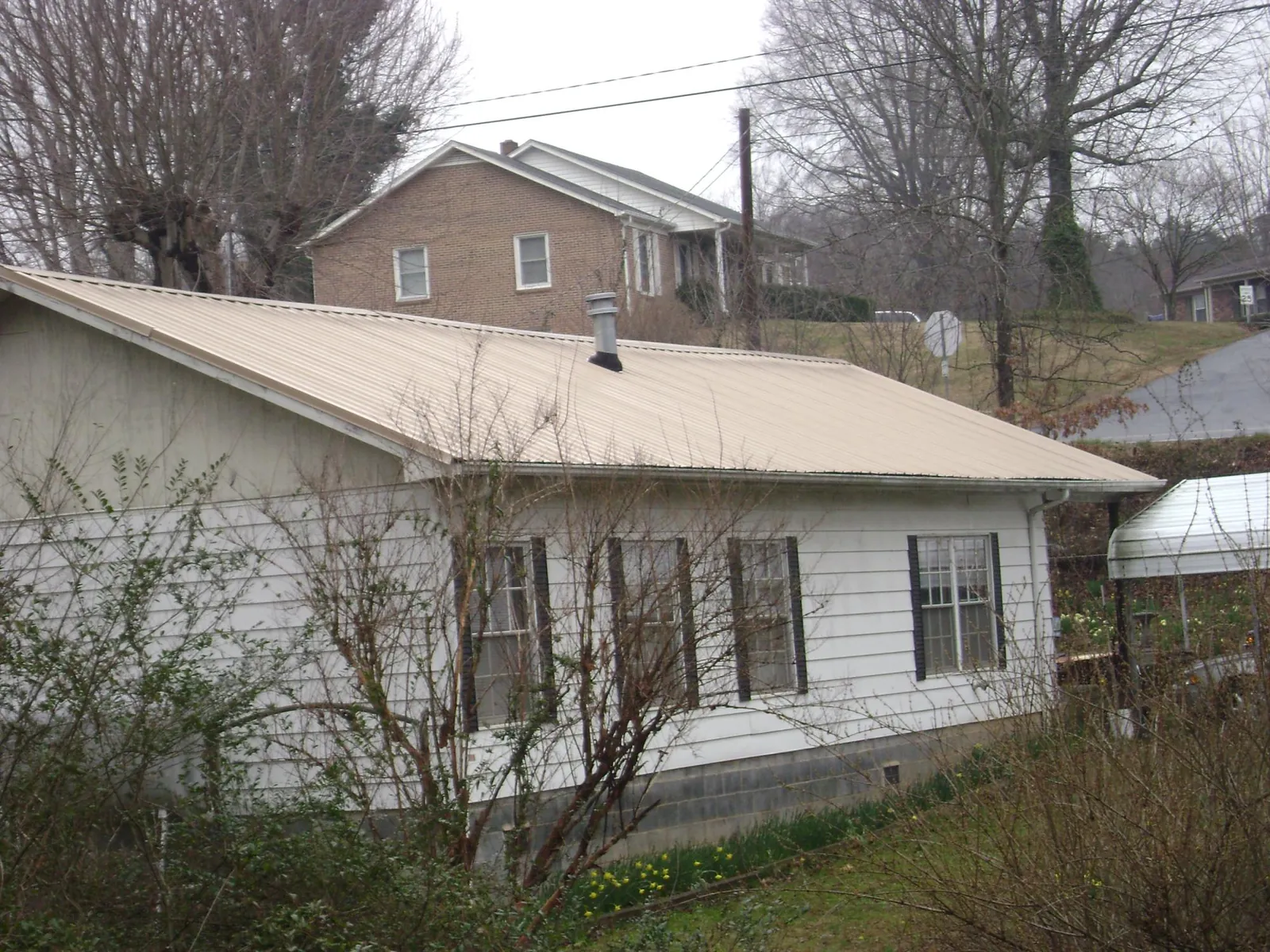 Tan metal roof on a white sided house set into a hillside — Commercial Roofing by Roofing Brothers in Blandon