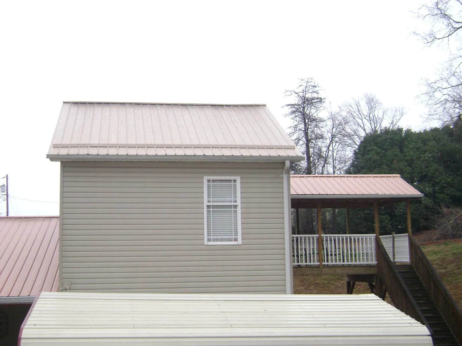 Tan metal roofs on a two story addition and attached porch, from a Roof Replacement job in Blandon